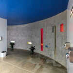 Unknown Architect’s Shower House Parque da Cidade showcasing a clean, minimalist interior with concrete walls, composite material ceiling, cylindrical light fixtures, and tiled plaster surfaces.