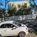 Unknown Architect’s Villa Avenida Sacadura Cabral showcasing a modern residential design with a sleek façade, featuring a parked Fiat 500 hatchback with visible car door, bumper, and hubcap in the foreground.