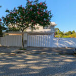 Unknown Architect’s Villa IV Rua Júlio Dantas showcasing a modern home with a gated entrance, landscaped driveway, palm trees, woody plants, and a shaded walkway bordered by home fencing.