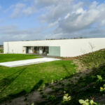 Nuno Graça Moura’s design of the 2 Villas at Bom Sucesso Resort showcasing modern landscaping with hedges, grass, and open land lots surrounding the plain architectural structures.
