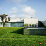 Nuno Graça Moura’s 8 Villas at Bom Sucesso Resort showcasing modern architecture with landscaped gardens, expansive lawns, and integrated outdoor living spaces surrounded by green yards and shaded areas.
