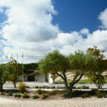 Nuno Graça Moura’s Golf Clubhouse at Bom Sucesso Resort showcasing a modern design with landscaped gardens, flagstone walkways, pebble paths, and shaded areas surrounded by shrubs and woody plants.