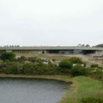 Nuno Graça Moura’s Golf Clubhouse at Bom Sucesso Resort showcasing a modern design with a glass façade integrated into the surrounding wetland, shrubland, chaparral, and riparian zone landscape.