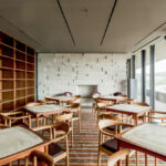 Nuno Graça Moura’s Golf Clubhouse at Bom Sucesso Resort showcasing an interior with wood flooring, composite material furniture, stained wood tables and chairs, and a modern restaurant design.