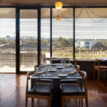Nuno Graça Moura’s Golf Clubhouse at Bom Sucesso Resort showcasing an interior with wooden furniture, hardwood flooring, dining tables and chairs, and a ceiling with modern architectural detailing.