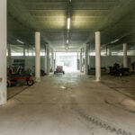 Nuno Graça Moura’s Golf Maintenance Building at Bom Sucesso Resort showcasing a concrete hall with composite material columns, expansive flooring, and daylighting illuminating the shaded parking lot.