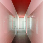 Nuno Graça Moura’s Tennis Club at Bom Sucesso Resort showcasing a symmetrical interior with red composite material walls, pink tiled flooring, and a ceiling featuring modern architectural finishes.