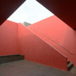 Nuno Graça Moura’s Tennis Club at Bom Sucesso Resort showcasing a modern design with concrete and composite material floors, triangular structural elements, orange and red accents, and angular stairs casting dynamic shadows.