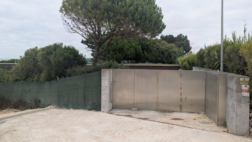 Álvaro Siza Vieira’s Casa do Pego showcasing a minimalist concrete structure with clean lines, integrated into the natural soil landscape and surrounded by simple home fencing.