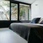 Antonio Corte-Real’s Maison de Vacances Esposende interior showcasing a minimalist bedroom with wooden flooring, a neatly made bed with white bedding, and simple furniture against a clean wall.