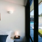 Antonio Corte-Real’s Maison de Vacances Esposende showcasing a bedroom with daylighting, featuring a minimalist wall and ceiling design, complemented by modern light fixtures and lampshades.