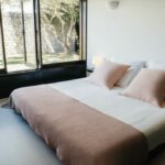Antonio Corte-Real’s Maison de Vacances Esposende interior showcasing a modern bedroom with minimalist design, featuring a neatly made bed with white linens, wooden flooring, and natural light enhancing the cozy home atmosphere.