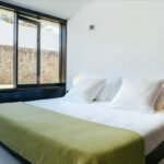 Antonio Corte-Real’s Maison de Vacances Esposende interior showcasing a modern bedroom with a minimalist bed frame, crisp linens, pillows, and a clean ceiling design.
