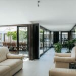 Antonio Corte-Real’s Maison de Vacances Esposende showcasing a modern interior with wood flooring, minimalist furniture including a couch, high ceiling, and large door openings in a bright living room.