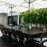 Antonio Corte-Real’s Maison de Vacances Esposende showcasing a modern outdoor patio with sleek furniture, an umbrella providing shade, a table and chairs arranged for dining, and decorative flowerpots with houseplants.