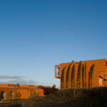Atelier dos Remédios, Madalena Cardoso de Menezes, and Francisco Teixeira Bastos’ 18 Red Row Houses at Bom Sucesso Resort featuring a brutalist architecture style with orange façades illuminated by evening sunlight casting long shadows.