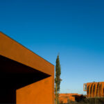 Atelier dos Remédios, Madalena Cardoso de Menezes, and Francisco Teixeira Bastos’ 18 Red Row Houses at Bom Sucesso Resort featuring a linear arrangement of vibrant red façades with large windows, set against an evening horizon with warm sunlight and long shadows.