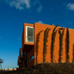 Atelier dos Remédios, Madalena Cardoso de Menezes, and Francisco Teixeira Bastos’ 18 Red Row Houses at Bom Sucesso Resort featuring vibrant orange composite material façades with modern urban design elements illuminated by sunlight.