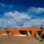 Atelier dos Remédios, Madalena Cardoso de Menezes, and Francisco Teixeira Bastos’ 18 Red Row Houses at Bom Sucesso Resort featuring vibrant orange façades, modern building materials, and dynamic shadows cast across the structures.