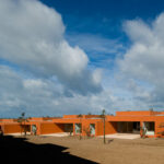 Atelier dos Remédios, Madalena Cardoso de Menezes and Francisco Teixeira Bastos’ 18 Red Row Houses at Bom Sucesso Resort featuring vibrant orange façades, modern building materials, and dynamic shadows cast across the structures.