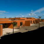 Atelier dos Remédios, Madalena Cardoso de Menezes, and Francisco Teixeira Bastos’ 18 Red Row Houses at Bom Sucesso Resort featuring vibrant orange façades with sharp shadows highlighting the modern, linear design.
