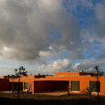 Atelier dos Remédios, Madalena Cardoso de Menezes, and Francisco Teixeira Bastos’ 18 Red Row Houses at Bom Sucesso Resort featuring vibrant orange façades with sharp shadows highlighting the linear arrangement and modern design elements.