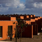 Atelier dos Remédios, Madalena Cardoso de Menezes, and Francisco Teixeira Bastos’ design of the 18 Red Row Houses at Bom Sucesso Resort featuring vibrant orange façades, modern building materials, and dynamic shadows cast across the structures.