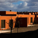 Atelier dos Remédios, Madalena Cardoso de Menezes, and Francisco Teixeira Bastos’ 18 Red Row Houses at Bom Sucesso Resort featuring vibrant orange façades with sharp shadows highlighting the linear arrangement of modern row houses.
