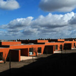 Atelier dos Remédios, Madalena Cardoso de Menezes, and Francisco Teixeira Bastos’ 18 Red Row Houses at Bom Sucesso Resort featuring vibrant orange façades with modern angular rooflines and large windows.
