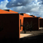 Atelier dos Remédios, Madalena Cardoso de Menezes, and Francisco Teixeira Bastos’ 18 Red Row Houses at Bom Sucesso Resort featuring vibrant orange façades with sharp shadows highlighting the linear arrangement of the modern row houses.