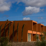 Atelier dos Remédios, Madalena Cardoso de Menezes, and Francisco Teixeira Bastos' 18 Red Row Houses at Bom Sucesso Resort featuring orange composite material façades with daylighting effects and distinct shadow patterns.