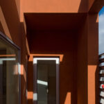 Atelier dos Remédios, Madalena Cardoso de Menezes, and Francisco Teixeira Bastos' 18 Red Row Houses at Bom Sucesso Resort featuring orange composite materials, concrete and plaster surfaces, wood-stained elements, and dynamic daylighting creating distinct shadows.