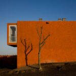 Atelier dos Remédios, Madalena Cardoso de Menezes, and Francisco Teixeira Bastos’ 18 Red Row Houses at Bom Sucesso Resort featuring vibrant orange façades, modern building materials, and dynamic shadows cast across the structures.