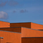 Atelier dos Remédios, Madalena Cardoso de Menezes, and Francisco Teixeira Bastos’ design of the 18 Red Row Houses at Bom Sucesso Resort featuring orange composite material façades with daylighting elements and modern building assemblies.