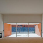 Atelier dos Remédios, Madalena Cardoso de Menezes, and Francisco Teixeira Bastos’ 18 Red Row Houses at Bom Sucesso Resort featuring brown composite material walls, concrete flooring, wood-stained elements, and ample daylighting.