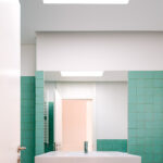 Atelier dos Remédios, Madalena Cardoso de Menezes, and Francisco Teixeira Bastos' design of the 18 Red Row Houses at Bom Sucesso Resort showcasing a modern bathroom interior with ceramic tiles, a clean white sink, chrome tap, and sleek plumbing fixtures under a tiled ceiling.