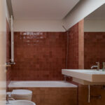 Atelier dos Remédios, Madalena Cardoso de Menezes, and Francisco Teixeira Bastos' design of the 18 Red Row Houses at Bom Sucesso Resort showcasing interior design with brown tiled flooring, composite material walls, and modern bathroom plumbing fixtures.