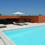 Atelier dos Remédios, Madalena Cardoso de Menezes, and Francisco Teixeira Bastos’ 6 Casa I Villas at Bom Sucesso Resort featuring a modern composite material structure with a glass façade, outdoor furniture including sunloungers and umbrellas, a swimming pool, and shaded resort seating areas.
