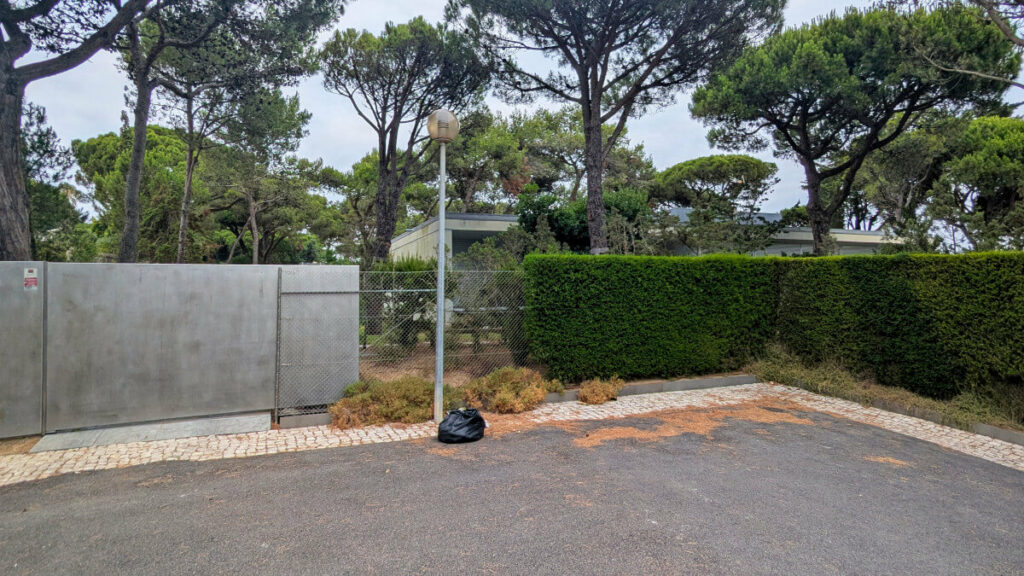 Eduardo Souto de Moura’s Casa em Cascais showcasing a modern home with clean lines, surrounded by landscaped shrubs, hedges, a gated fence, and a shaded walkway.