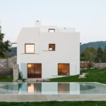 Guilherme Machado Vaz’s House in Afife showcasing a modern farmhouse design with a pitched roof, white exterior walls, and large windows blending traditional and contemporary elements.