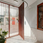 Manuel Gomes da Costa’s The Modernist Faro showcasing a minimalist design with a wood-stained hardwood floor, composite material walls, metal accents, concrete structural elements, and a modern gate integrated into the façade.