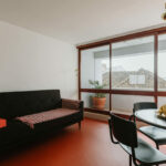 Manuel Gomes da Costa’s The Modernist Faro interior showcasing wood flooring, minimalist furniture, and clean-lined walls in a bright living room with a high ceiling.