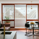 Manuel Gomes da Costa’s The Modernist Faro interior showcasing wood-stained flooring, ceiling panels, minimalist furniture, and a warm, modern apartment room design.