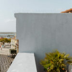 Manuel Gomes da Costa’s Modernist Faro showcasing a concrete and plaster façade with blue walls, balconies adorned with flowerpots and houseplants, and surrounding palm trees.