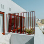 Manuel Gomes da Costa’s Modernist Faro showcasing a sleek apartment building with balconies featuring handrails, shaded areas, and houseplants enhancing daylighting.