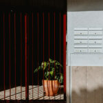 Manuel Gomes da Costa’s The Modernist Faro showcasing a red composite material façade with metal and concrete elements, wood-stained accents, a painted gate, and a houseplant visible near the entrance.