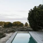 Manuel Aires Mateus’s Casas na Areia showcasing minimalist design with a rectangular swimming pool, hardwood planks, and modern outdoor furniture.