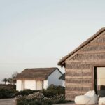 Manuel Aires Mateus’s Casas na Areia showcasing a natural material shed with a simple roof and hut-like structure.
