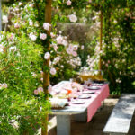 Casa Veiga / Casa Portufornia, Colares by Manuel Tainha, Rui Costa Martins (3777) Manuel Tainha and Rui Costa Martins' Casa Veiga / Casa Portufornia showcasing a modern structure with a glass façade, cantilevered upper level, and a landscaped backyard featuring pink flowers and shrubs in a spring garden setting.