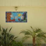 Casa Veiga / Casa Portufornia, Colares by Manuel Tainha, Rui Costa Martins (3748) Manuel Tainha and Rui Costa Martins' Casa Veiga / Casa Portufornia showcasing a modern painted wall with vibrant mural art, surrounded by palm trees and houseplants in floral pots.